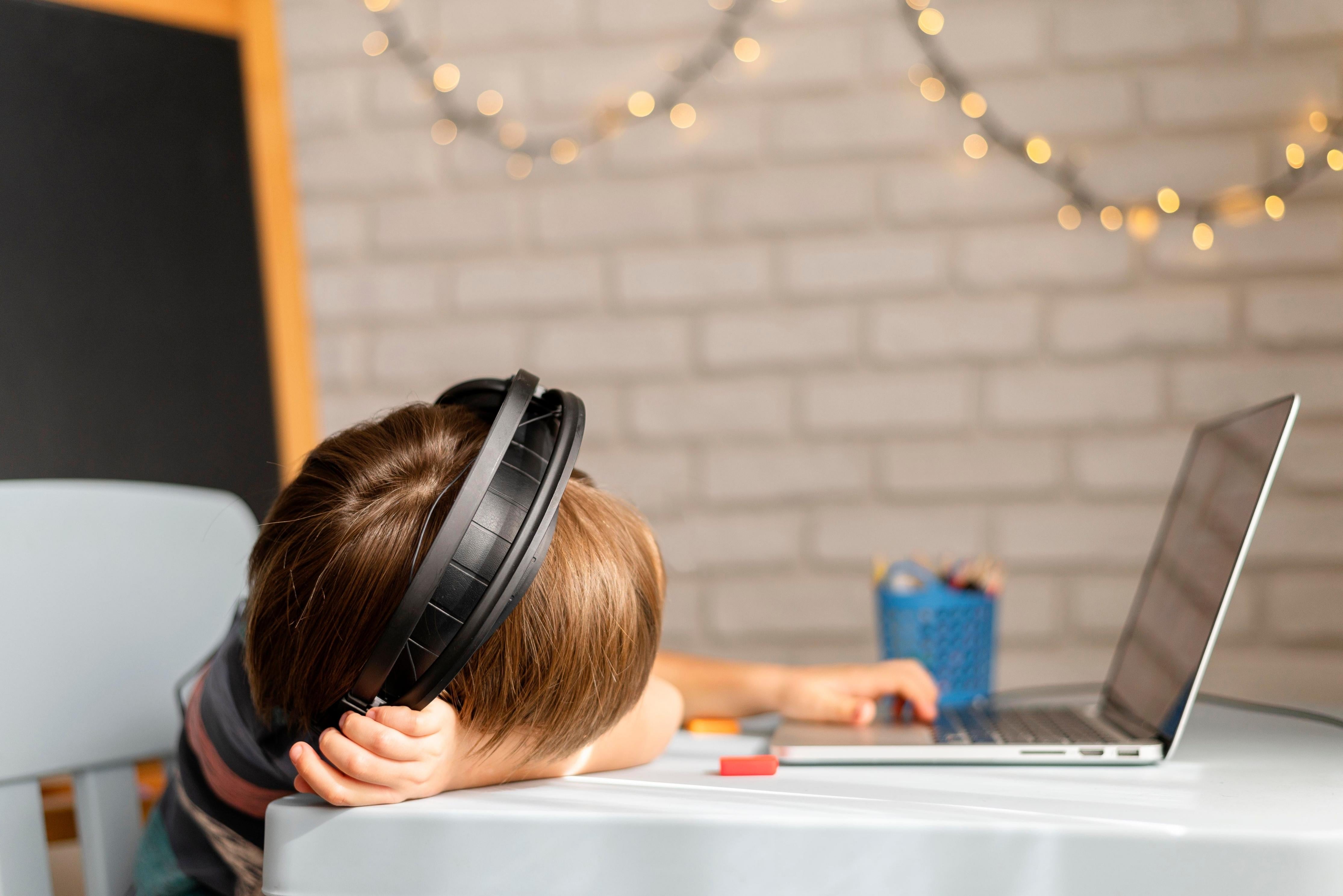 Boy with headphones resting his head on desk while using laptop