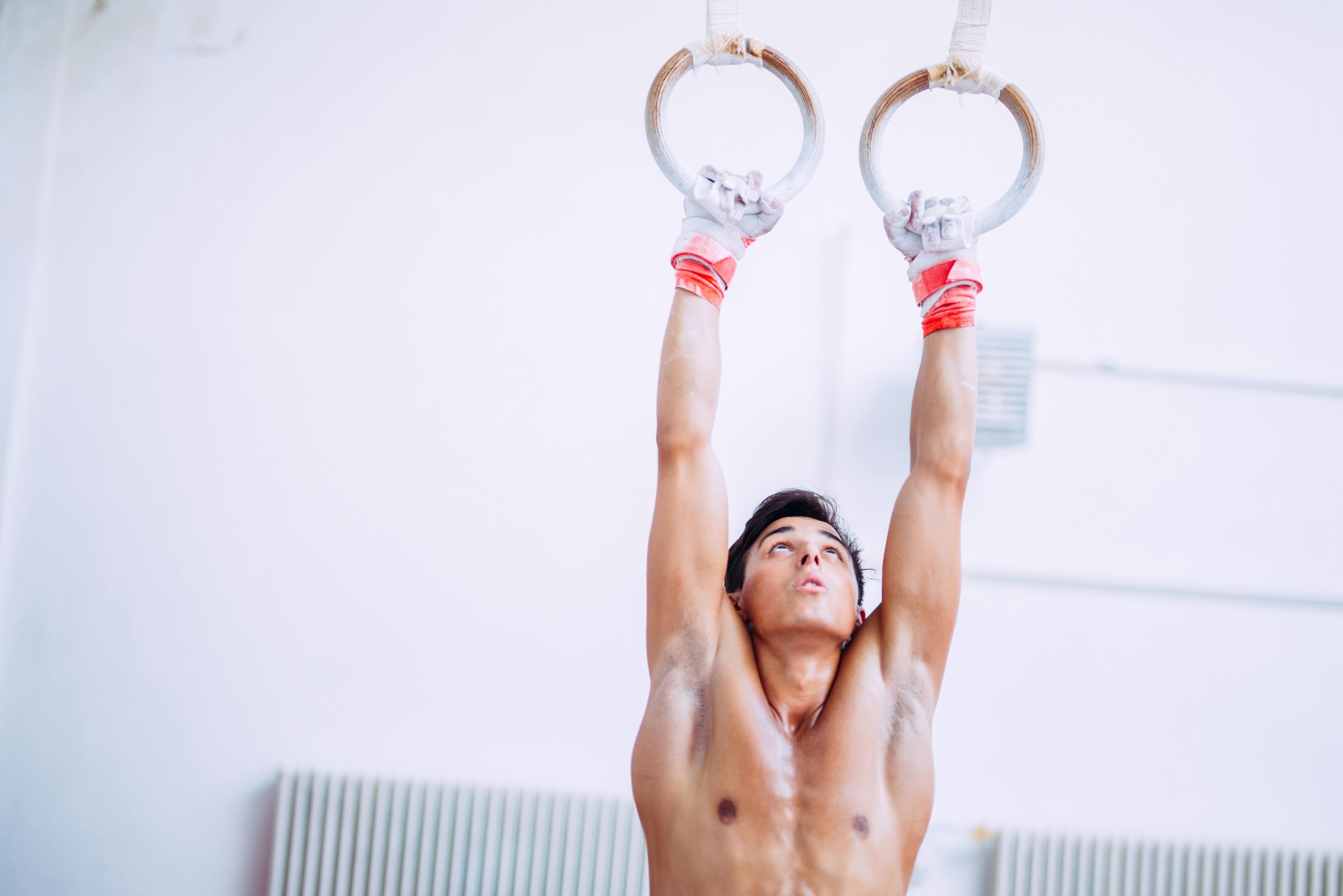 Strong fit man hanging from gymnastic rings